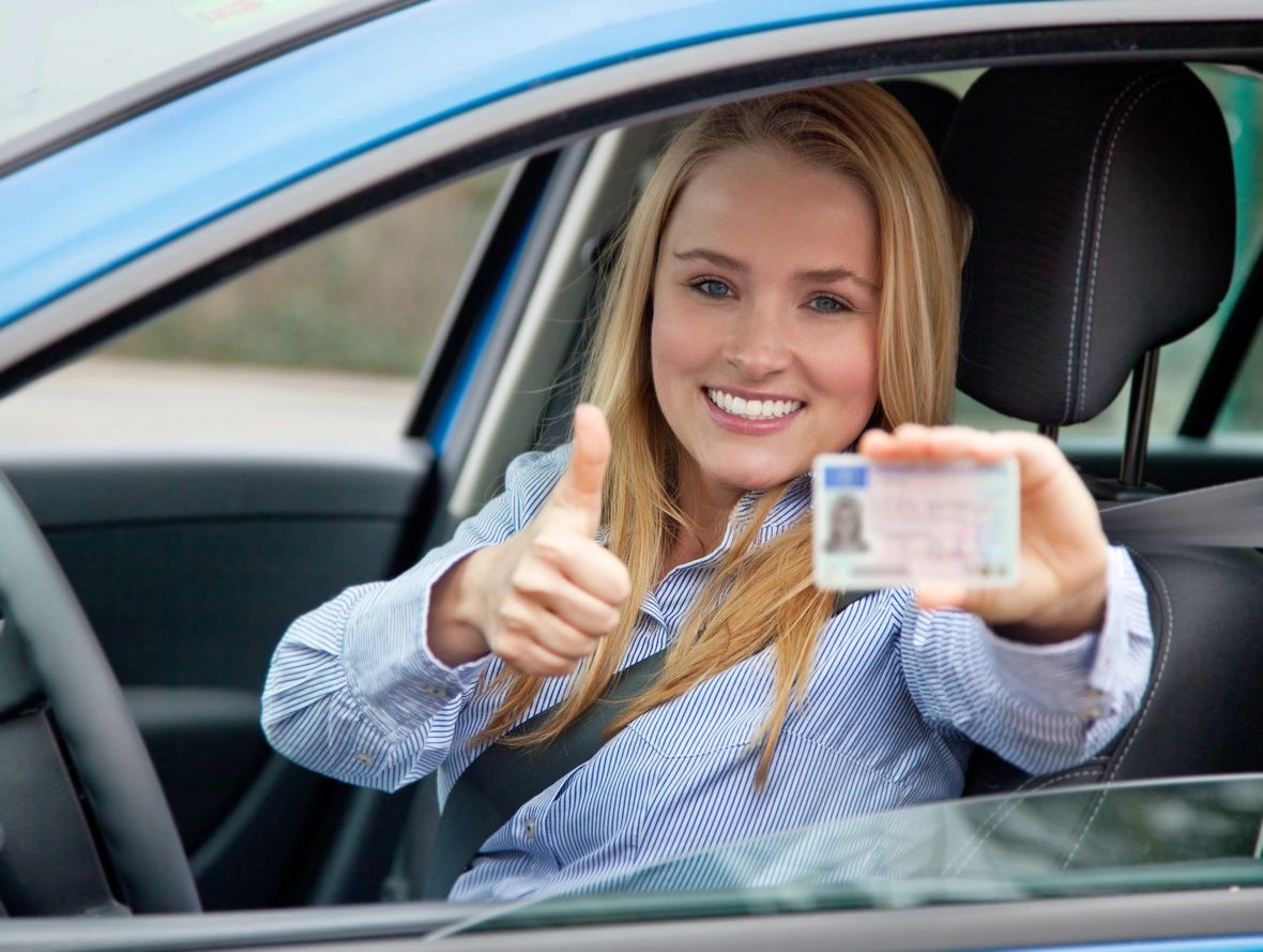 A woman in the drivers seat of her car holding up a license.